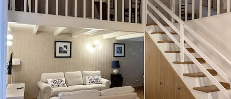 A spacious living area with a white staircase, a sofa set, and a wooden cabinet.