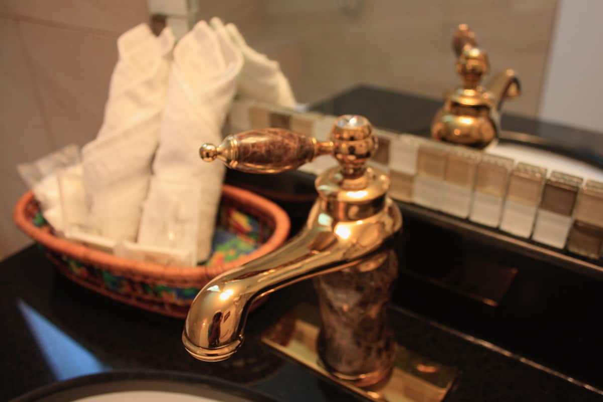 Een badkamer met een gouden kraan, een zeepbakje en een zeepdispenser.
