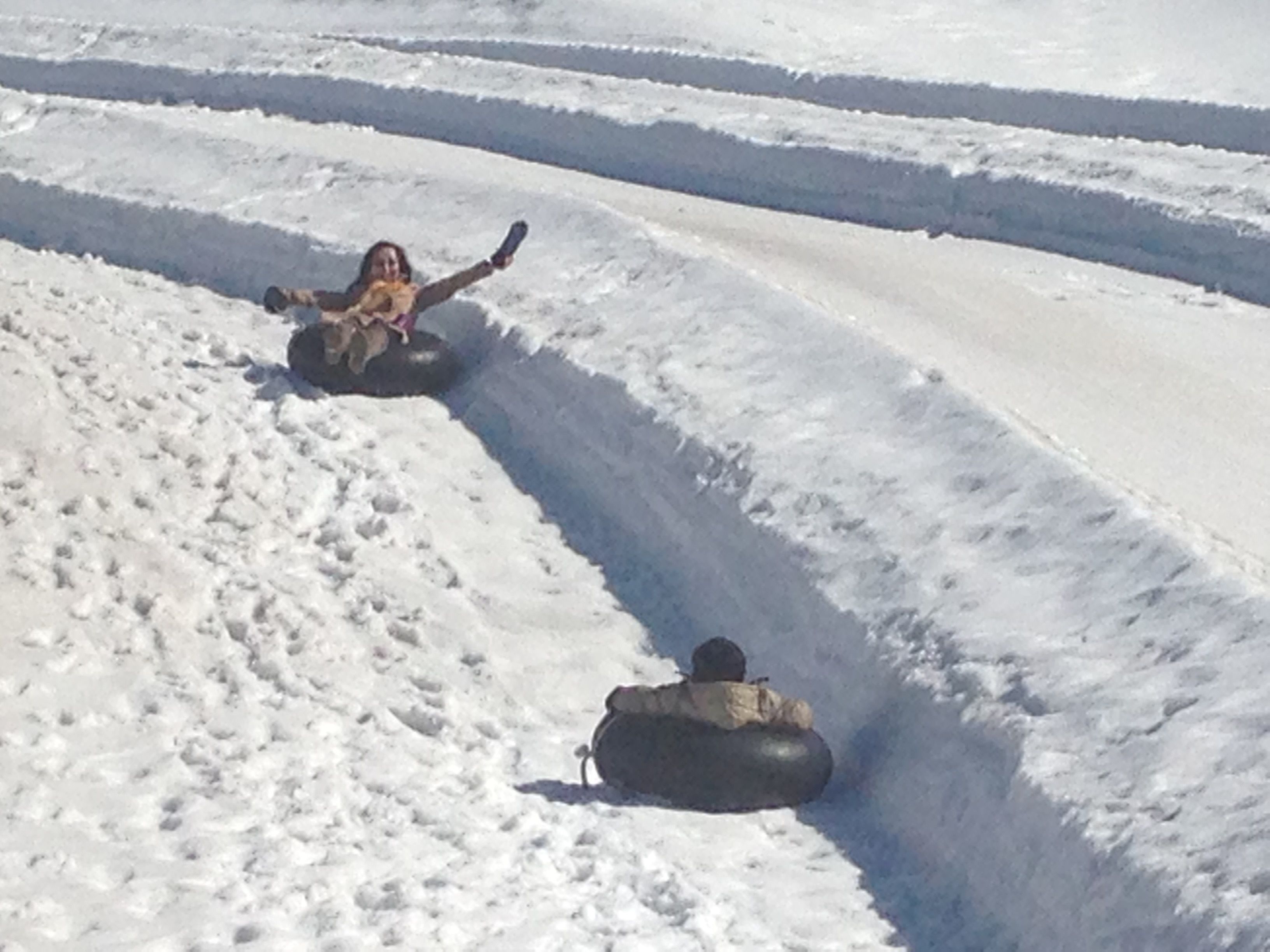 A snowy slope with people sliding down on snow tubes.