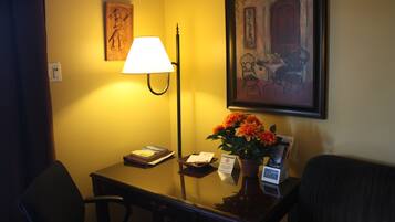 Una habitación de hotel con un escritorio, una lámpara, un cuadro enmarcado y un jarrón con flores.