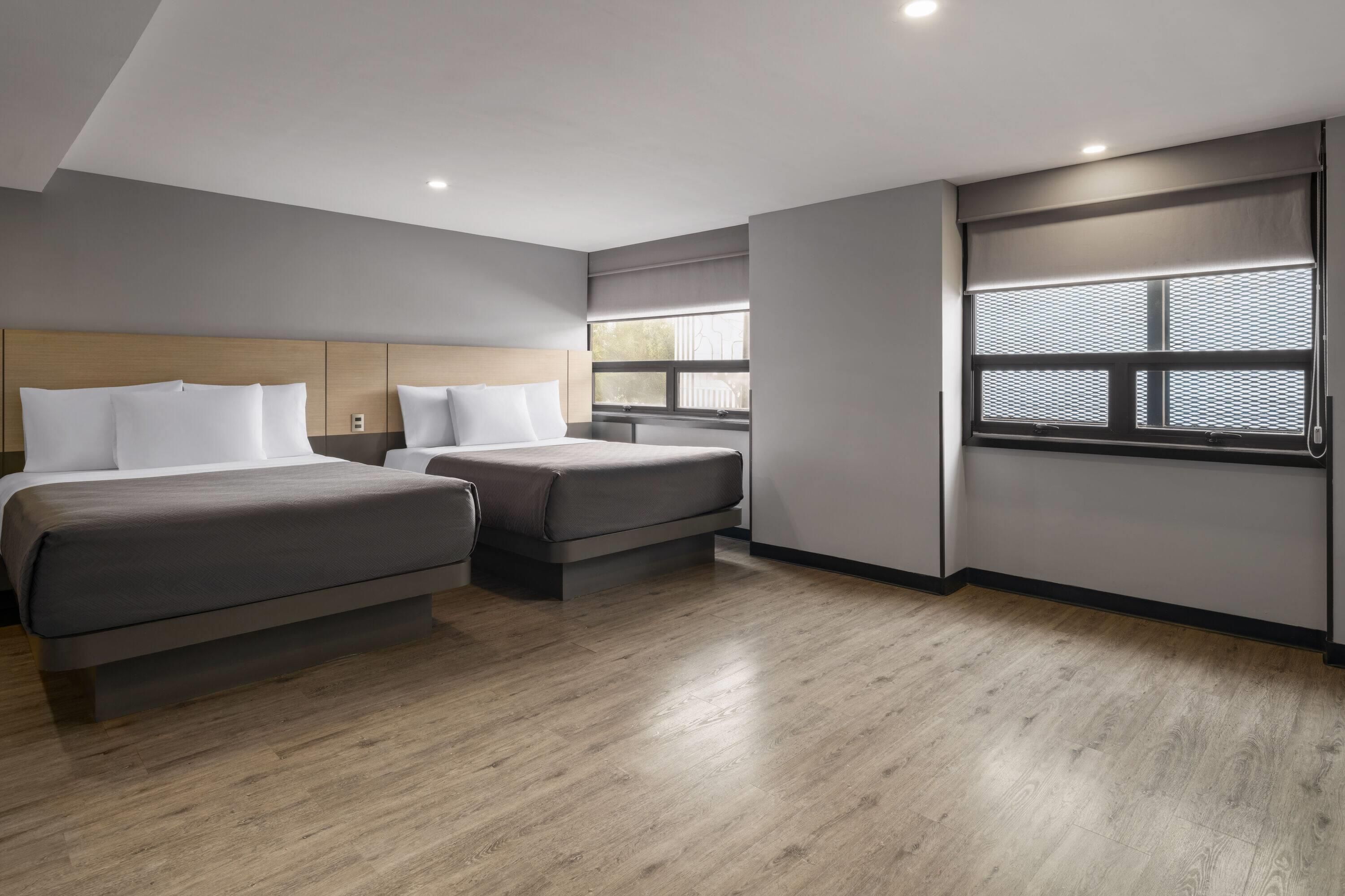 Habitación de hotel con dos camas, un ventanal con persianas y suelo de madera.