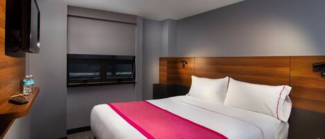Habitación de hotel con una cama grande, una mesita de noche con una botella de agua, un televisor montado en la pared y un cabecero de madera.