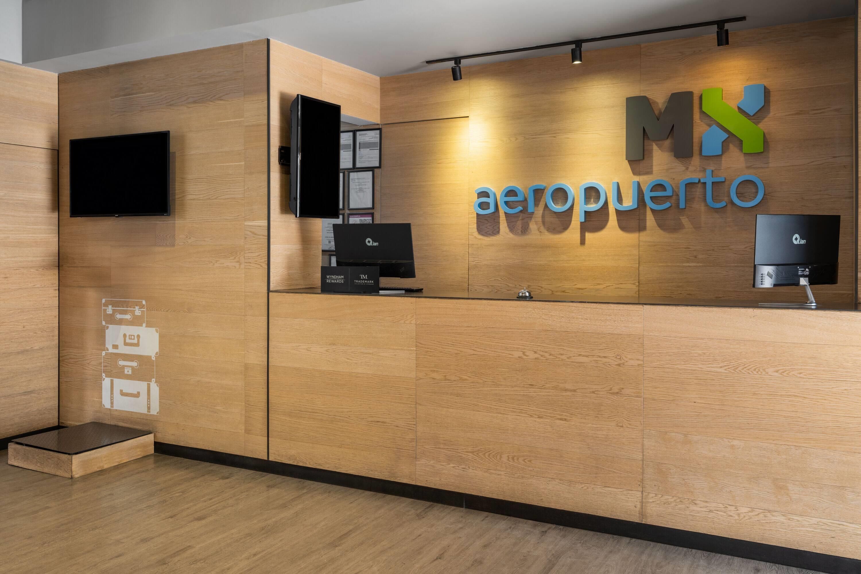 Una recepción con detalles de madera, un televisor de pantalla plana montado encima y un logotipo que dice 'MX aeroporto'.