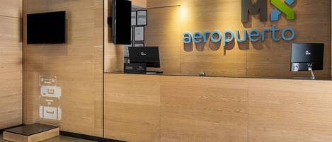 Una recepción con detalles de madera, un televisor de pantalla plana montado encima y un logotipo que dice 'MX aeroporto'.