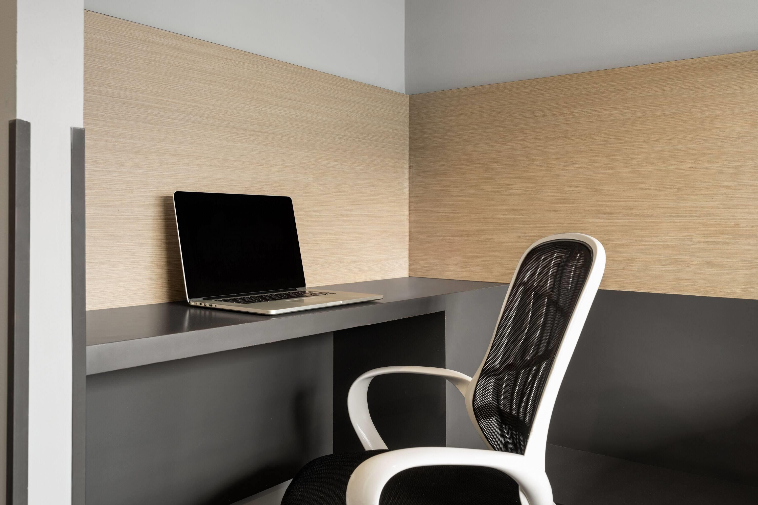 A modern office space with a laptop on a desk, a chair, and a partition wall.