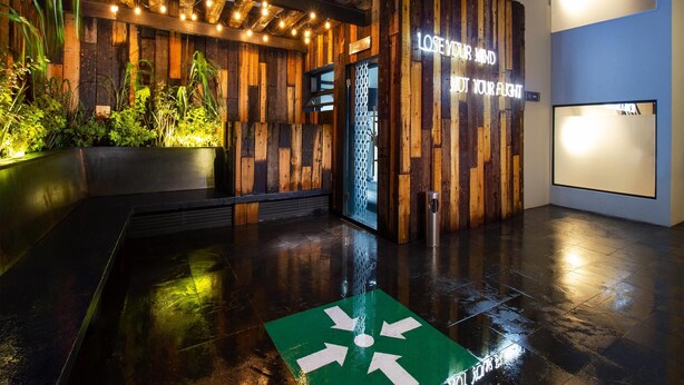 A modern building entrance with wooden paneling, a green directional sign, and a neon sign that reads "LOSE YOUR MIND, NOT YOUR FLEET".