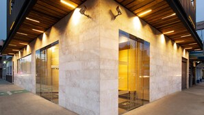 A modern building with a stone facade, large glass doors, and a wooden ceiling.