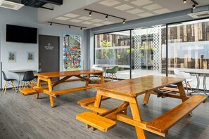 A modern meeting room with wooden tables and benches, a large window with a view of greenery, and a colorful poster on the wall. - Hotel MX aeropuerto CDMX, Trademark Collection by Wyndham (Mexico City)