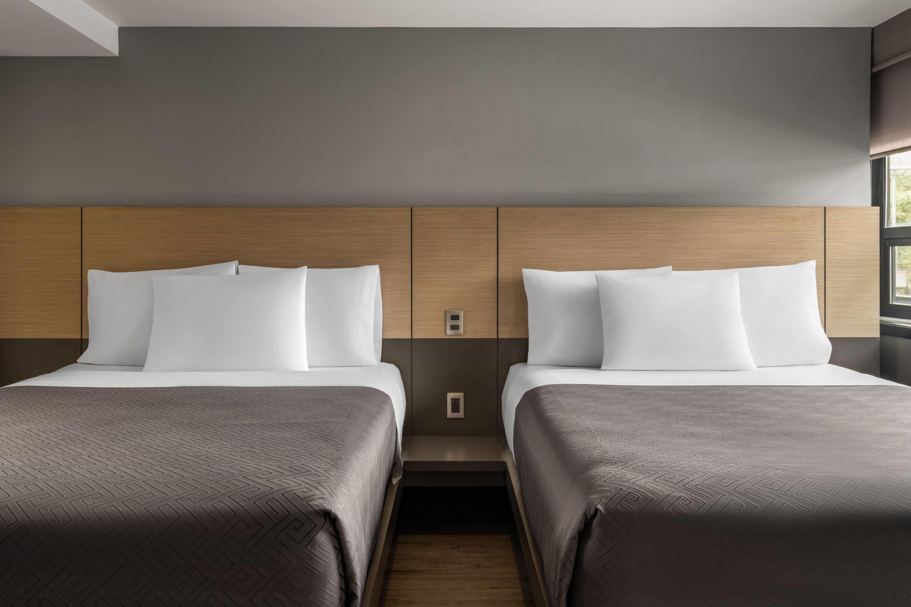 Een hotelkamer met twee bedden, een houten hoofdbord en een raam.