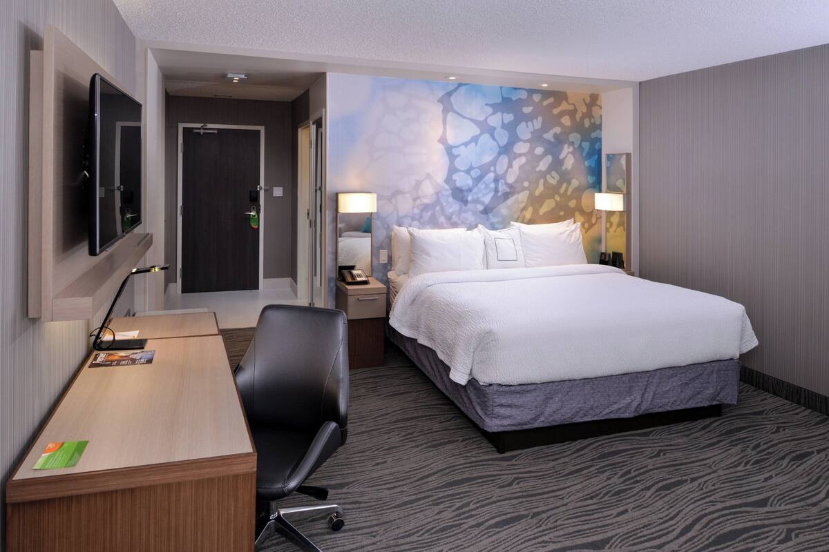 A hotel room with a bed, desk, chair, and a TV mounted on the wall.