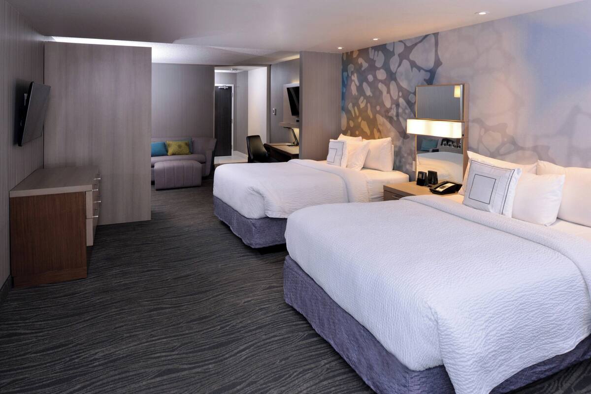A hotel room with two beds, a desk, a chair, a TV, and a mirror.