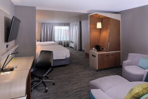 A hotel room with a desk, two beds, a TV, a desk lamp, a chair, a sofa, and a small seating area. - Courtyard by Marriott Saskatoon Airport (Saskatoon)