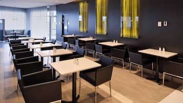 Een moderne eetruimte met meerdere tafels en stoelen, grote ramen met gele gordijnen, en een strak, eigentijds design.