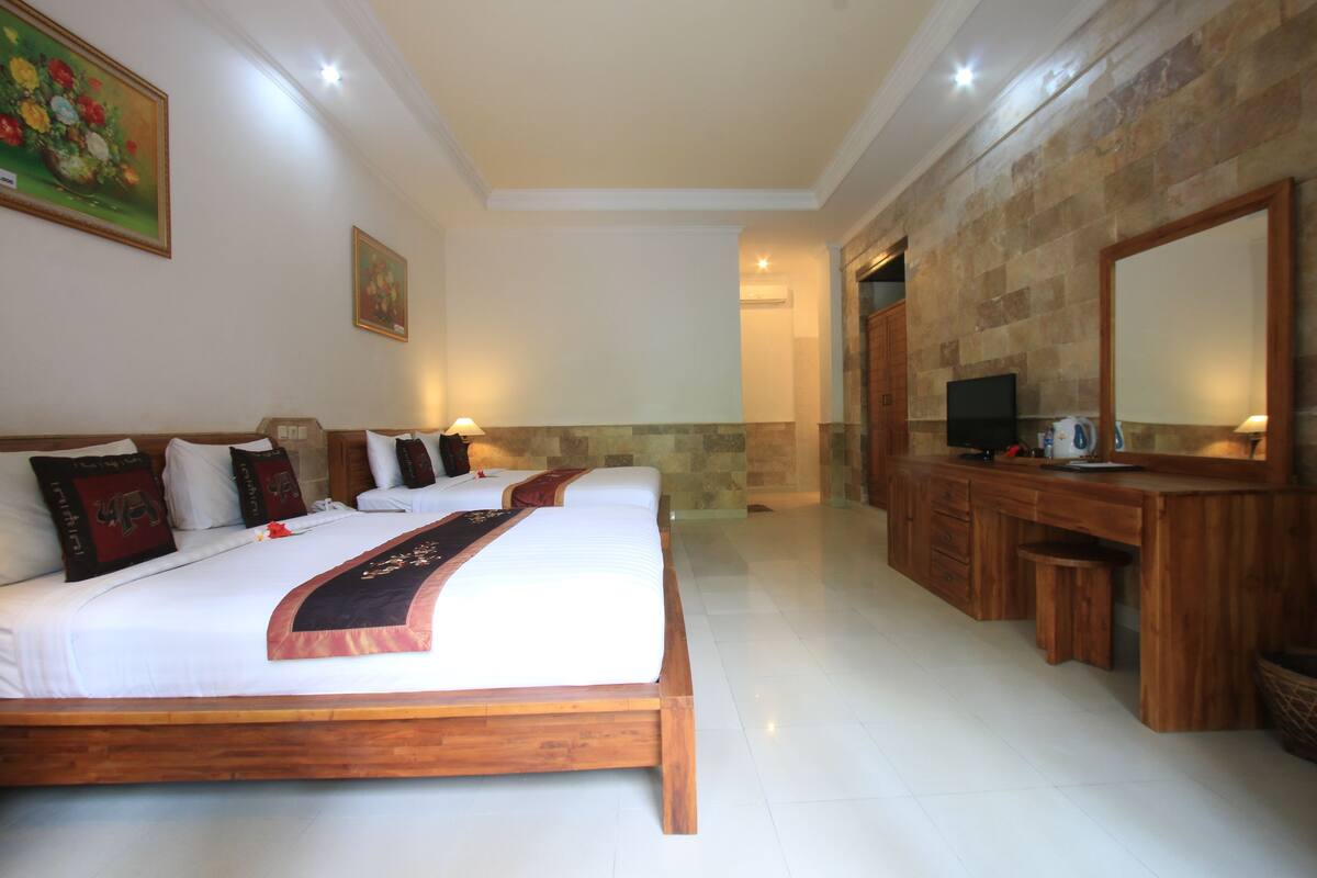 A hotel room with a large bed, a wooden desk, a television, and a stone wall.