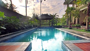 A swimming pool with a gazebo in the center, surrounded by lush greenery and a building with a balcony. - Alam Terrace Cottages (Ubud)