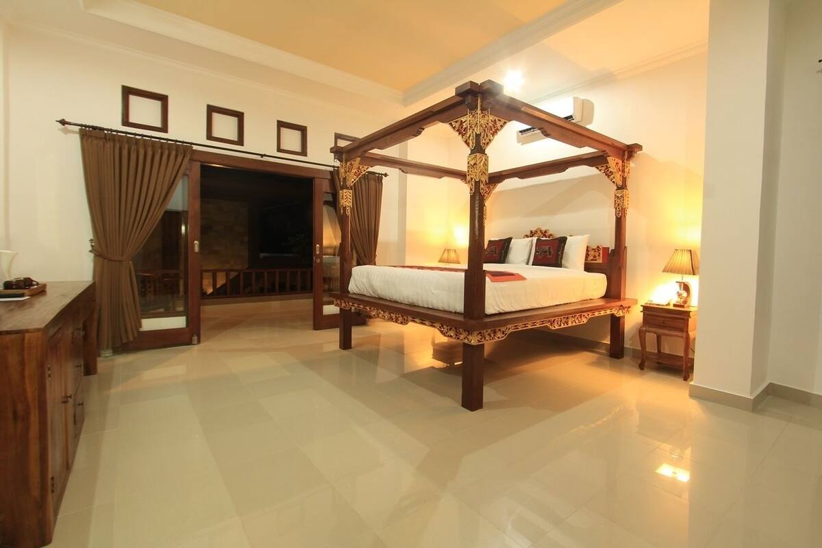 A spacious bedroom with a four-poster bed, a wooden desk, and a large mirror.