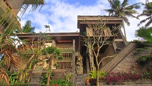 A traditional building with a stone staircase leading to a wooden door, surrounded by tropical plants and palm trees. - Alam Terrace Cottages (Ubud)
