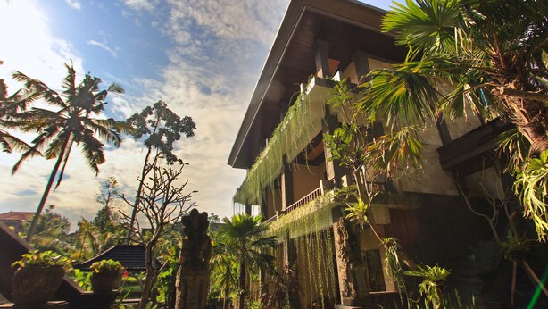 A building with a balcony and hanging plants, surrounded by palm trees and other greenery. - Alam Terrace Cottages (Ubud)