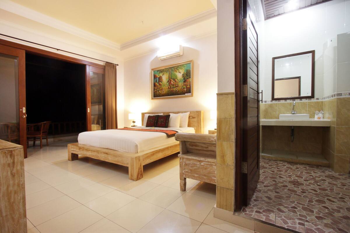 A hotel room with a bed, bedside table, and a bathroom with a sink and mirror.