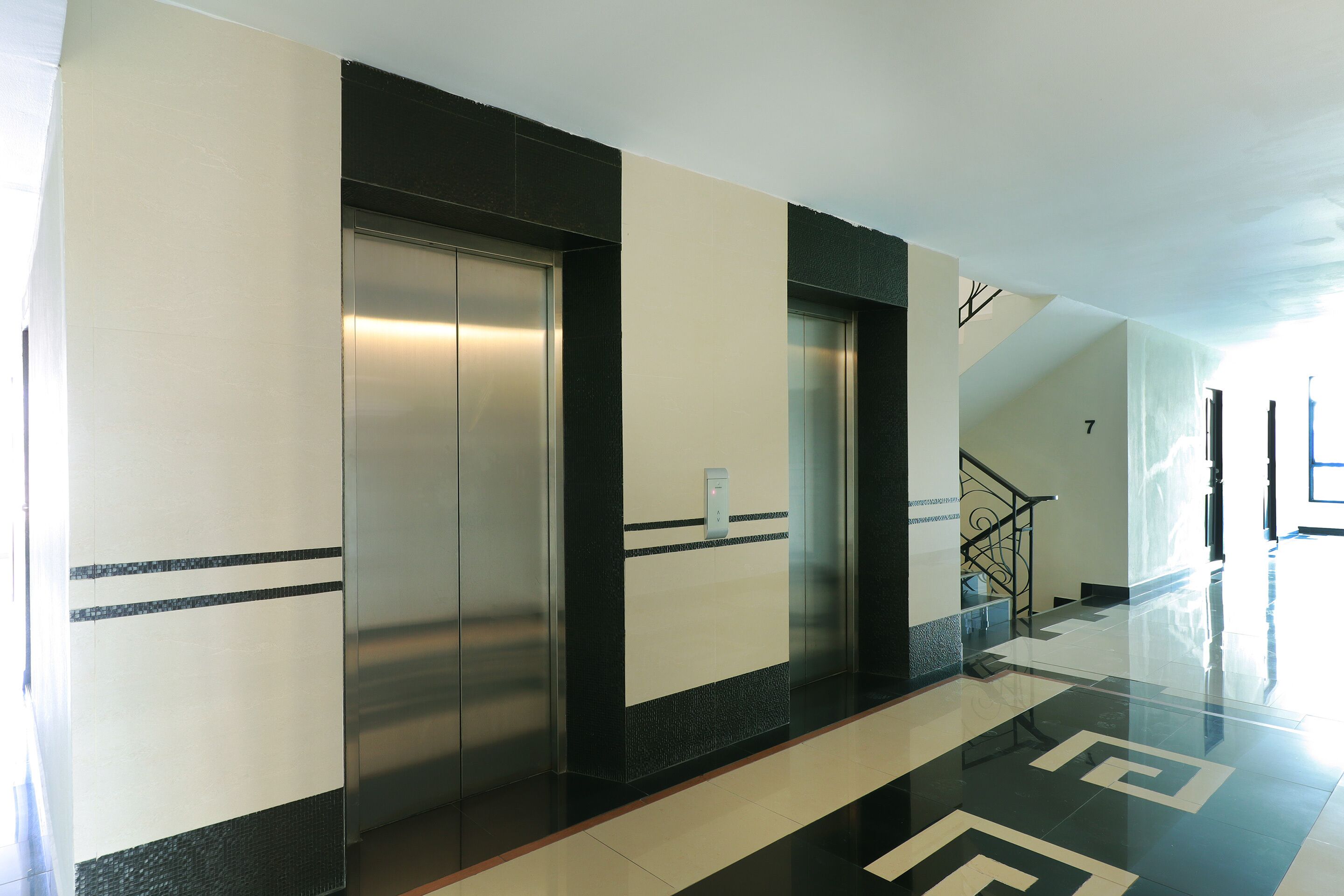 Een moderne lift met een metalen afwerking, een zwart-wit wandontwerp en een spiegelende vloer.