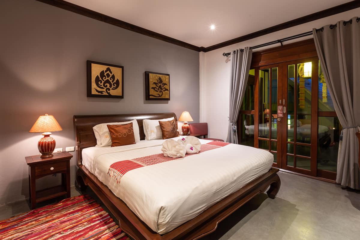 A hotel room with a large bed, two wall-mounted lamps, a red and white striped bedspread, and a red rug.