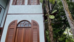 Un edificio con una puerta de madera grande, dos ventanas con persianas y una escalera que lleva a un nivel superior.