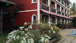 Un hotel de varios pisos con balcones, fachada roja y un jardín con flores blancas y rosas.
