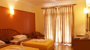 Habitación de hotel con dos camas, cabecera de madera, un escritorio con lámpara y un ventanal con cortinas.