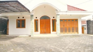 Une maison à deux étages, avec une façade blanche, un toit en tuiles et une allée d’entrée pavée.