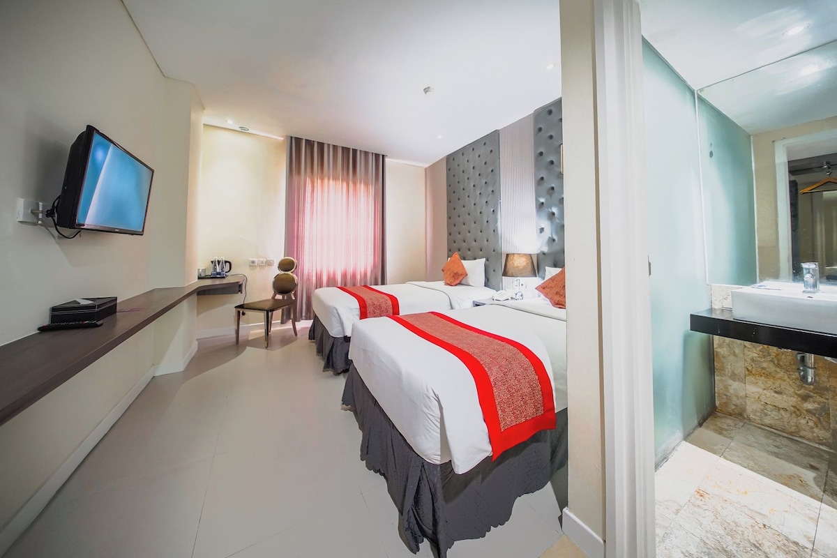 A hotel room with two beds, a TV, a desk, and a bathroom.