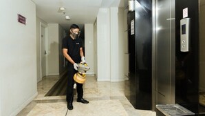 Eine Person in einer schwarzen Uniform bedient ein gelbes Gerät in einer Diele mit Marmorboden, einem Aufzug und einer Tür mit einem Schild.