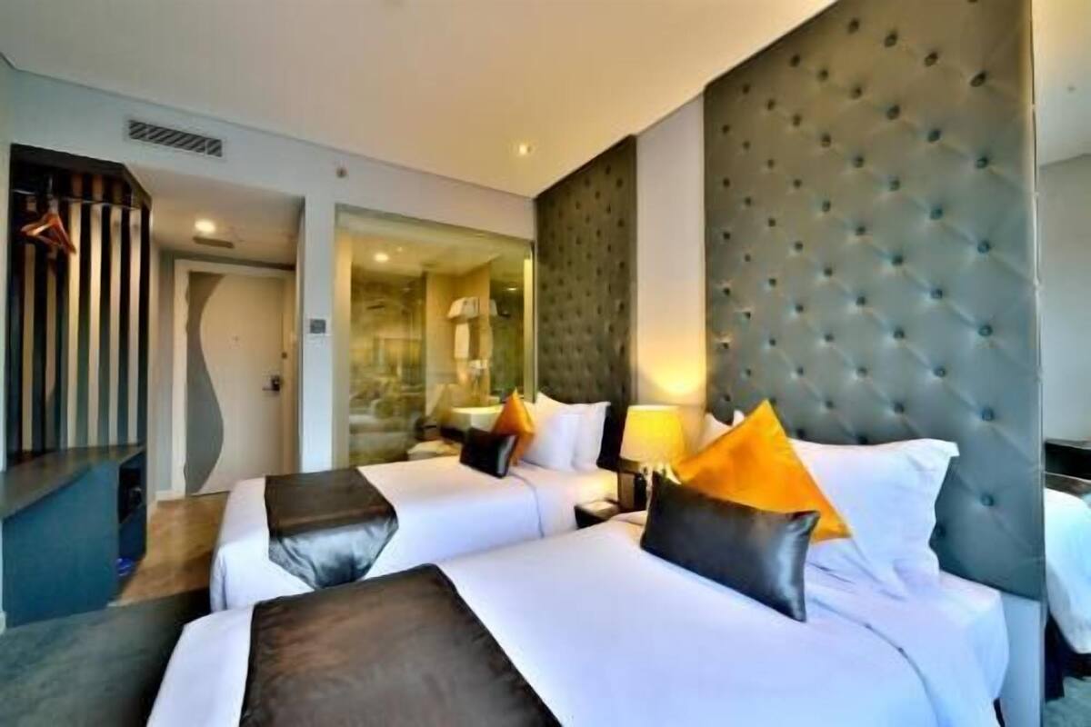 Ein Hotelzimmer mit zwei Betten, einem großen, gepolsterten Kopfteil und einem Spiegel.