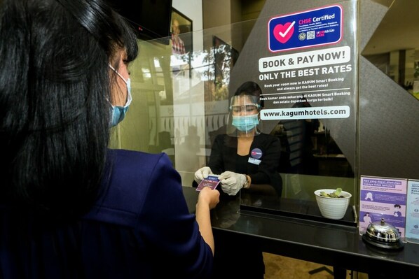 A person at a reception desk with a sign indicating CHSE certification and a booking prompt. - Serela Cihampelas Hotel (Bandung)