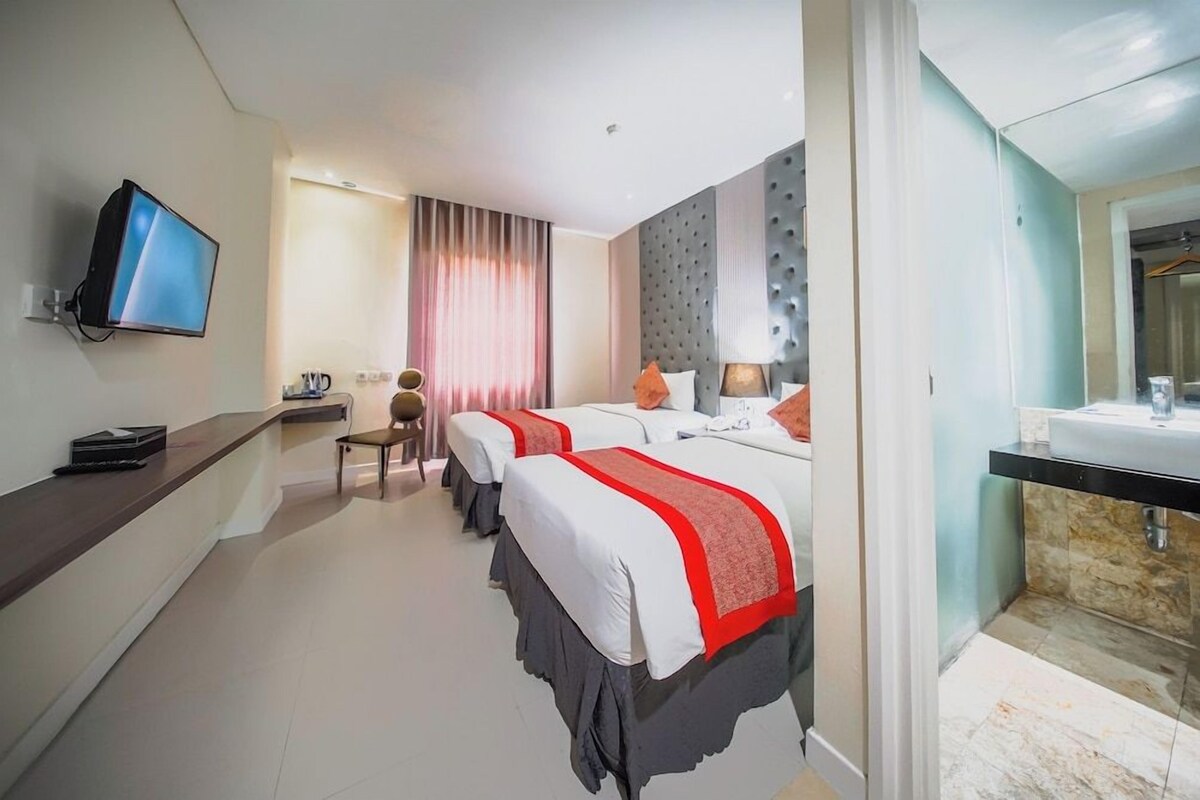 A hotel room with two beds, a television, a desk, a chair, and a bathroom.