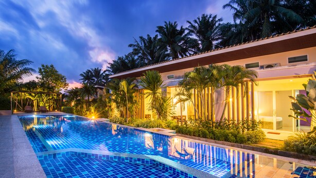 A swimming pool with a tiled edge, surrounded by palm trees and a building with a balcony. - The Fong Krabi Resort (Krabi)