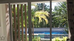 A bedroom with a large sliding glass door leading to a balcony with a view of a pool and palm trees. - The Fong Krabi Resort (Krabi)