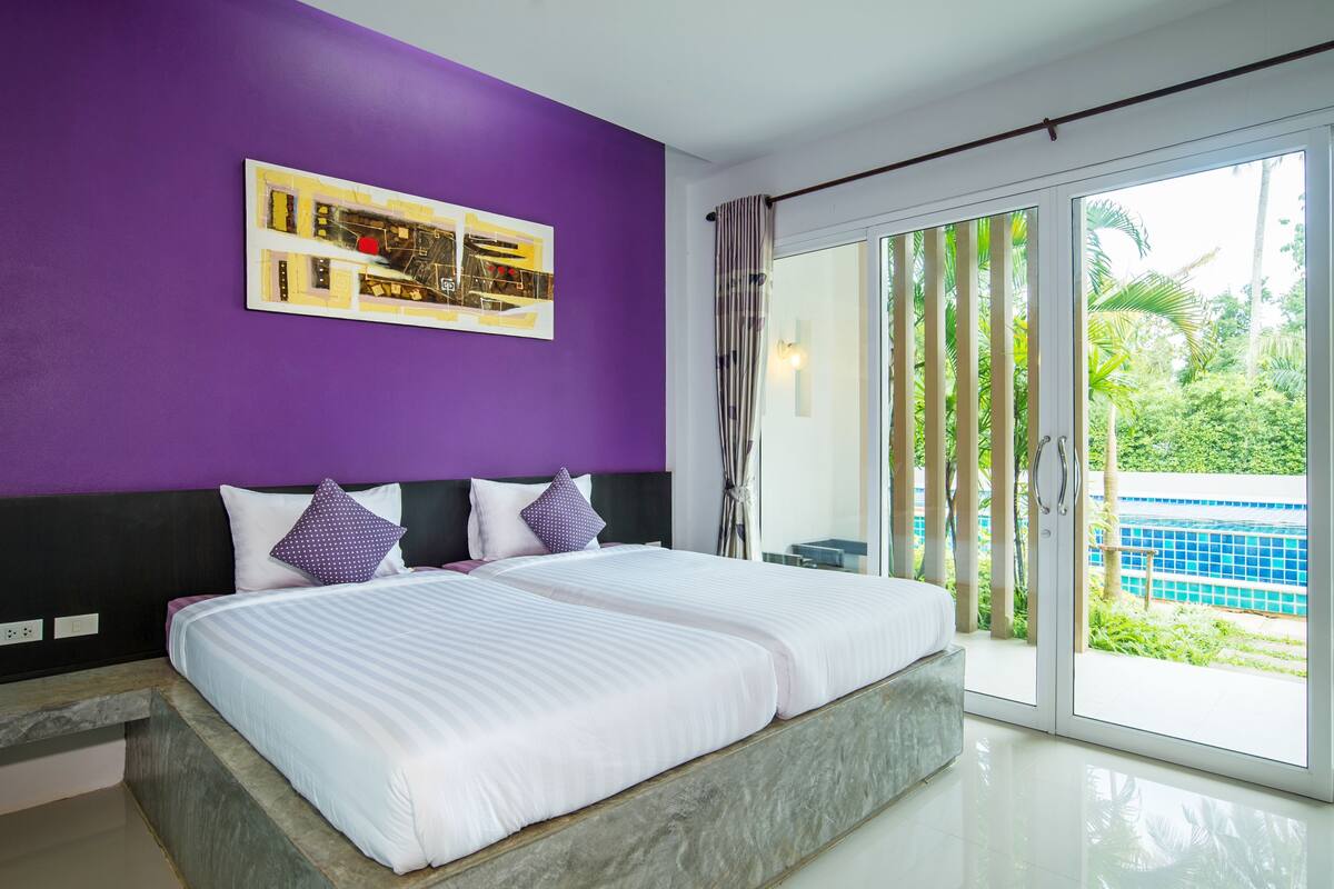 Une chambre moderne avec un grand lit, un mur d’accent violet et une vue sur une piscine.