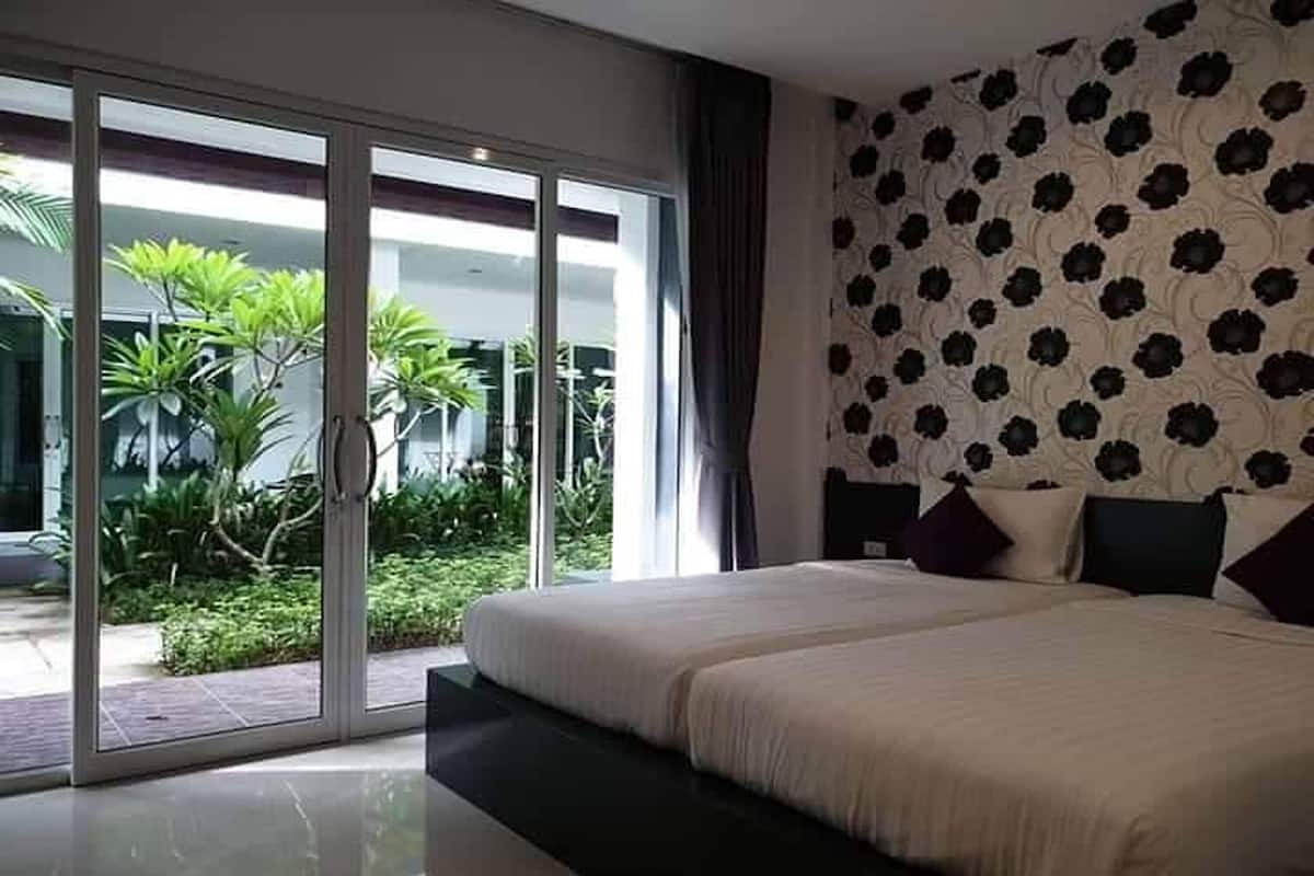 A bedroom with a large bed, a sliding glass door leading to a garden, and a patterned wall.