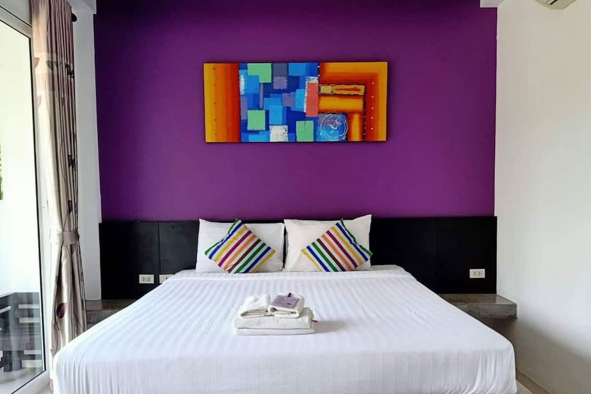 A hotel room with a large bed, white bedding, and a colorful abstract painting on the wall.