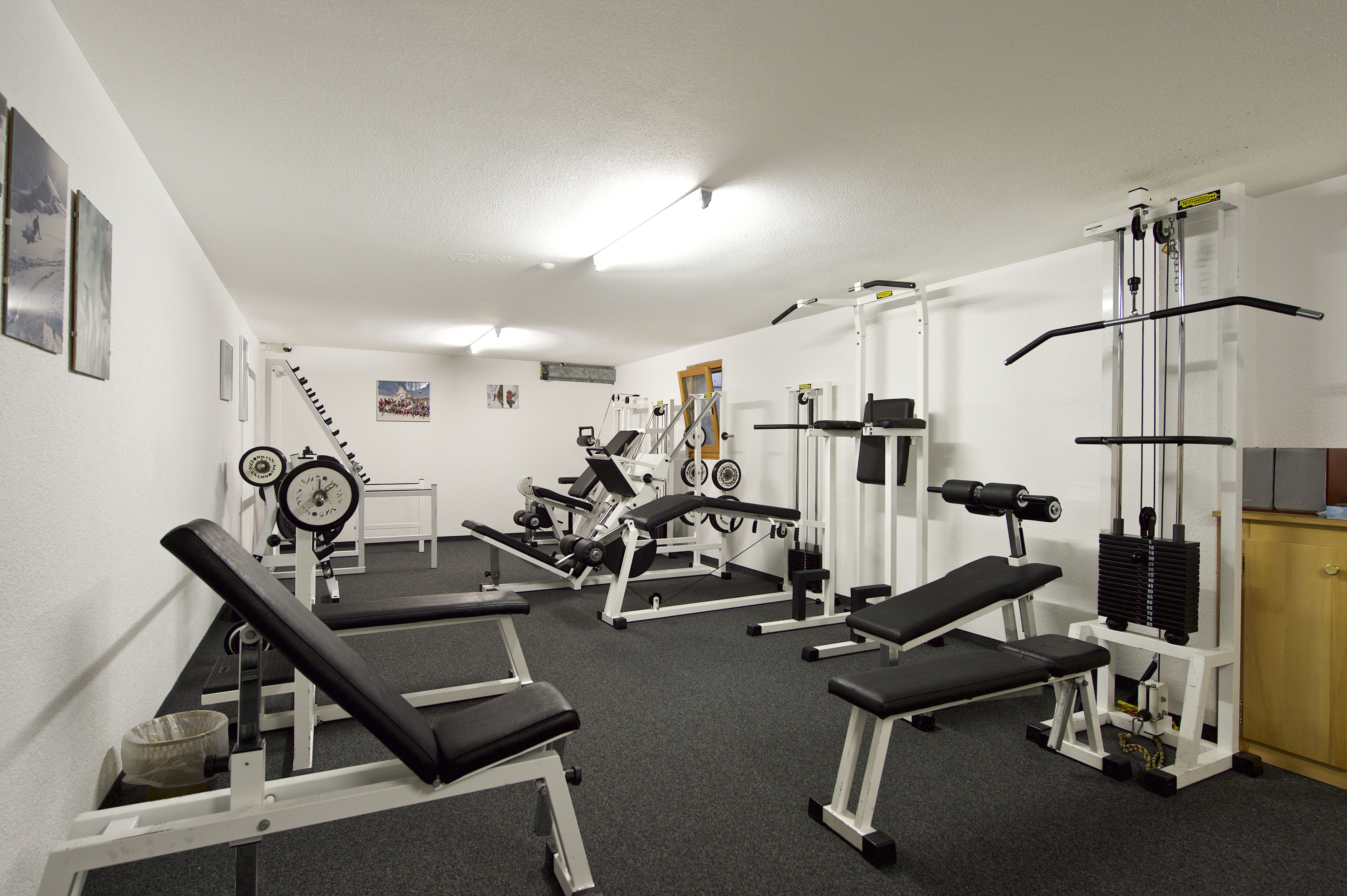 A gym with various exercise equipment, benches, and a staircase.