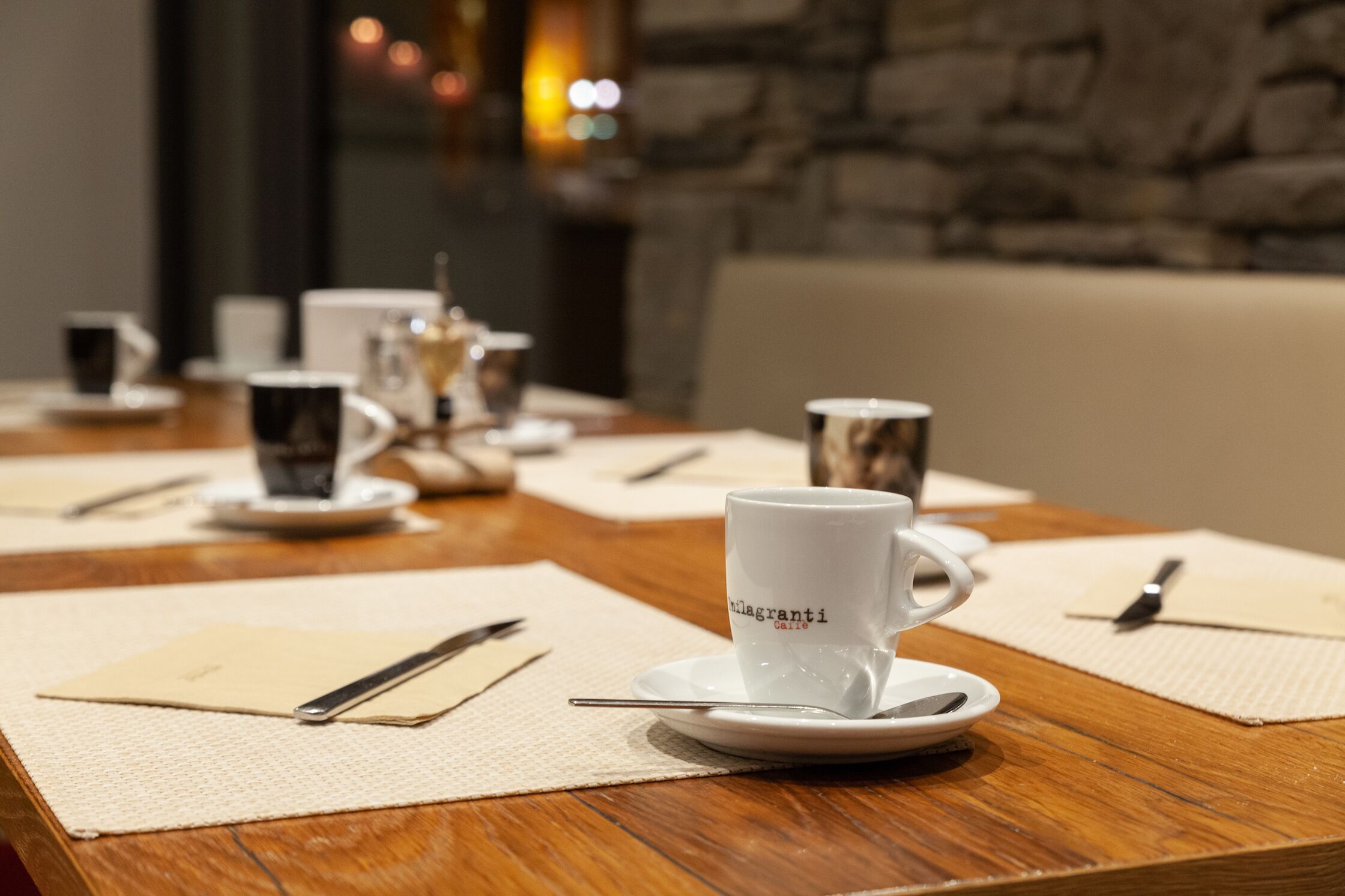 Un tavolo da pranzo con una tazza bianca con la scritta "Caffetteria" e un cucchiaino su un piattino, circondato da tovaglioli e posate.