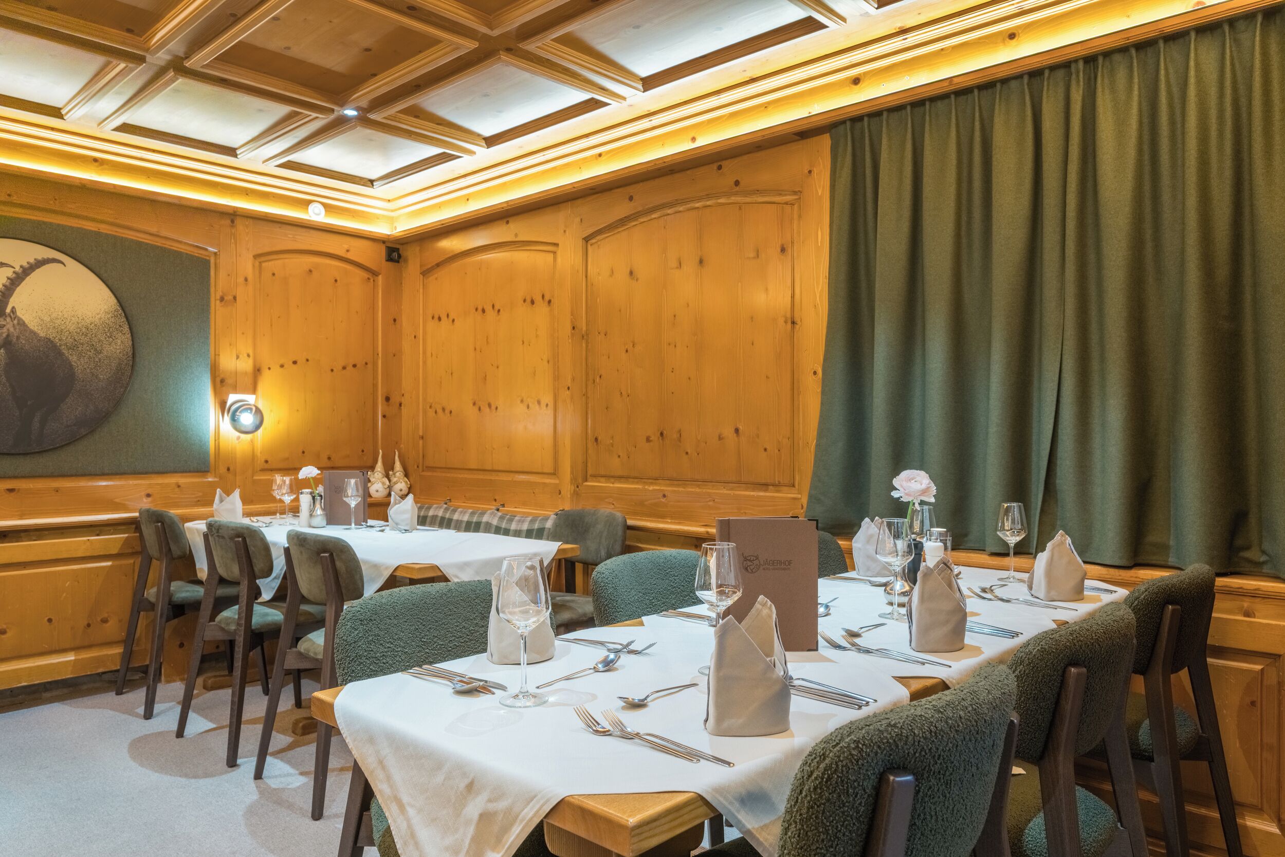 A conference room with wooden paneling, green upholstered chairs, white tablecloths, and a large painting on the wall.
