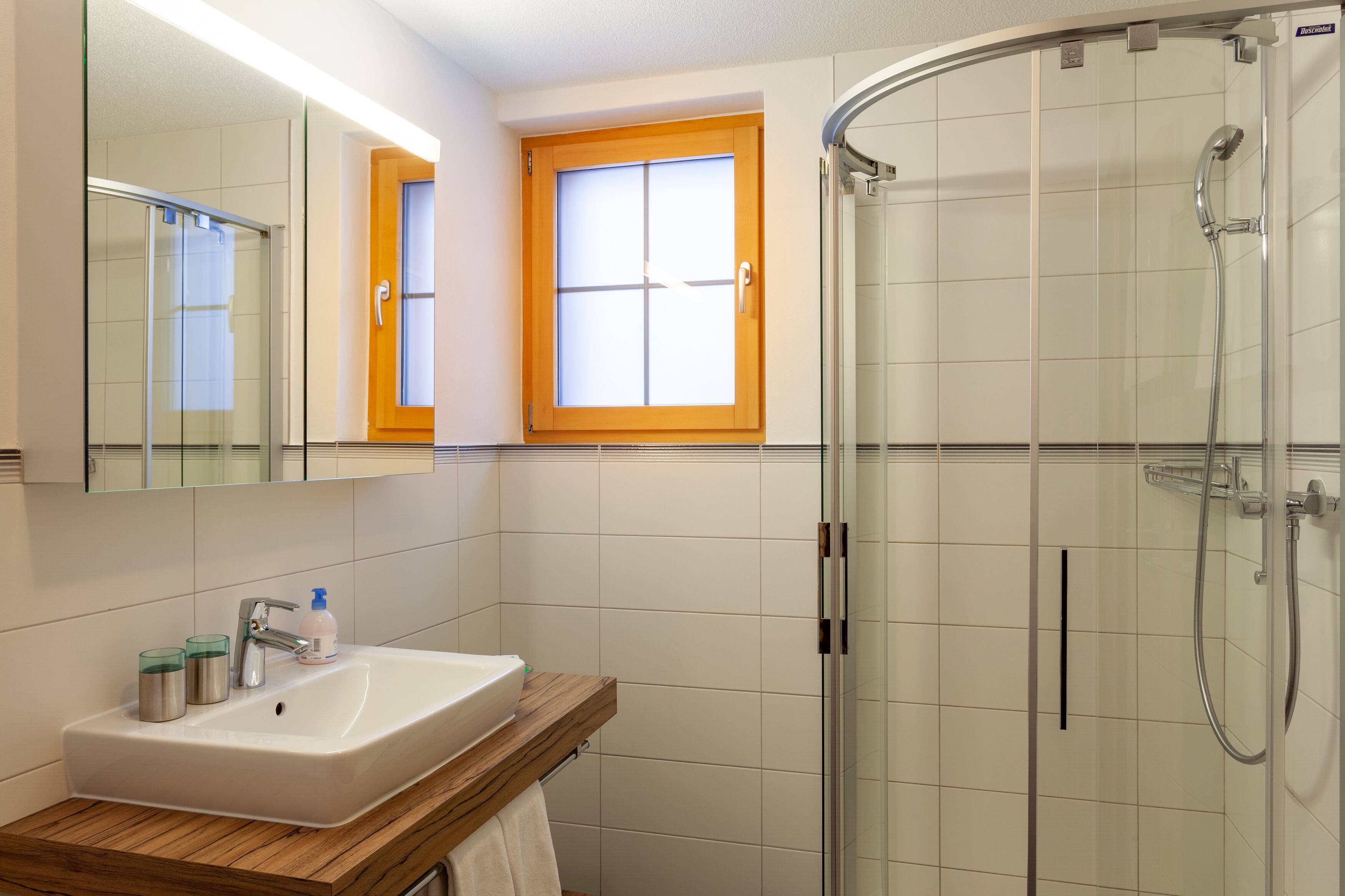 Ein modernes Badezimmer mit einer gläsernen Duschkabine, einem weißen Waschbecken mit Holzauskładung und einem Spiegel darüber.