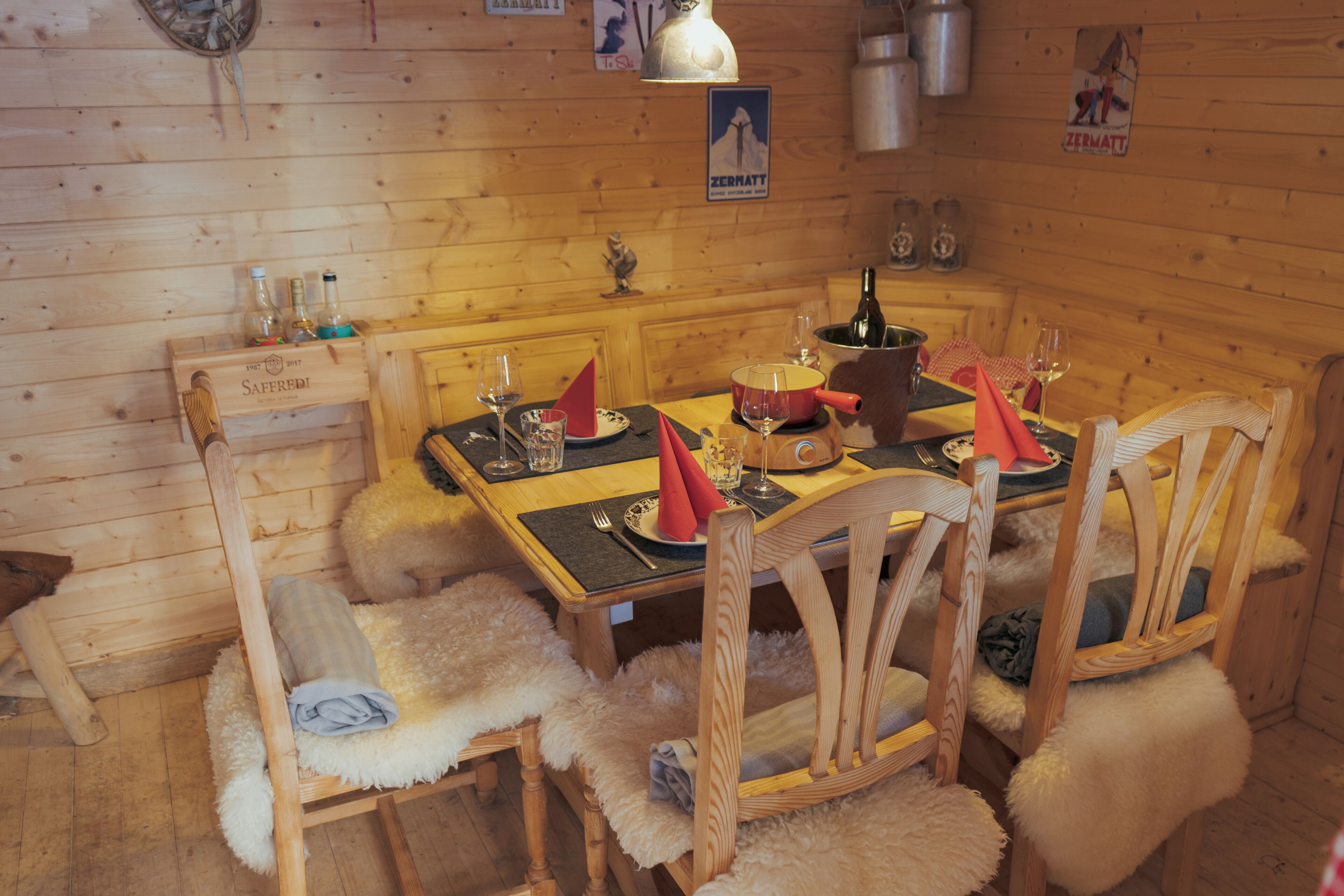 A wooden interior with a dining table set for four, surrounded by chairs with fur throws.