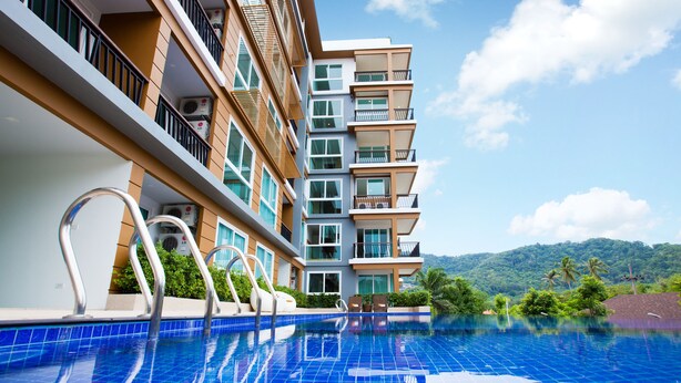 A modern hotel with a swimming pool, balconies, and a view of lush greenery. - Grand Nai Harn Suites (Rawai)