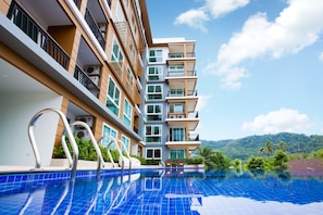 A modern hotel with a swimming pool, balconies, and a view of lush greenery. - Grand Nai Harn Suites (Rawai)