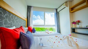 A hotel room with two beds, a large window, and a view of greenery. - Grand Nai Harn Suites (Rawai)