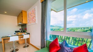 A modern kitchen with a dining area, a green sofa with colorful cushions, and a balcony with a scenic view. - Grand Nai Harn Suites (Rawai)