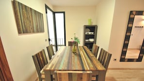 A dining area with a wooden table and chairs, a vase with flowers, and a bookshelf with plates and cups. - Living Sevilla Centro Maestranza (Seville)