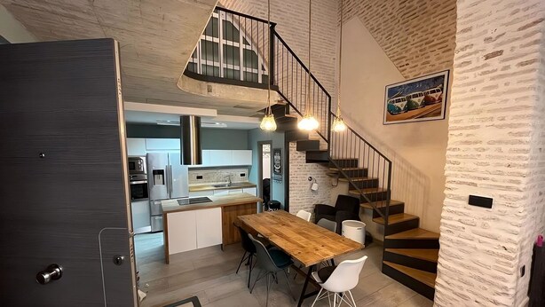 A modern kitchen with a wooden dining table, white chairs, and a staircase leading to an upper level. - Living Sevilla Centro Maestranza (Seville)